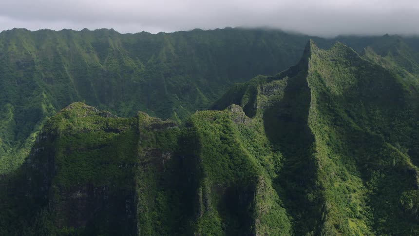 The camera is panning across the cliffs and peaks of the mountain that has the clouds meeting the peaks