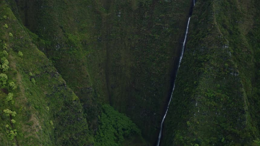 A thin waterfall cascades down a dark verdant cliff face barely visible against the densely vegetated slope