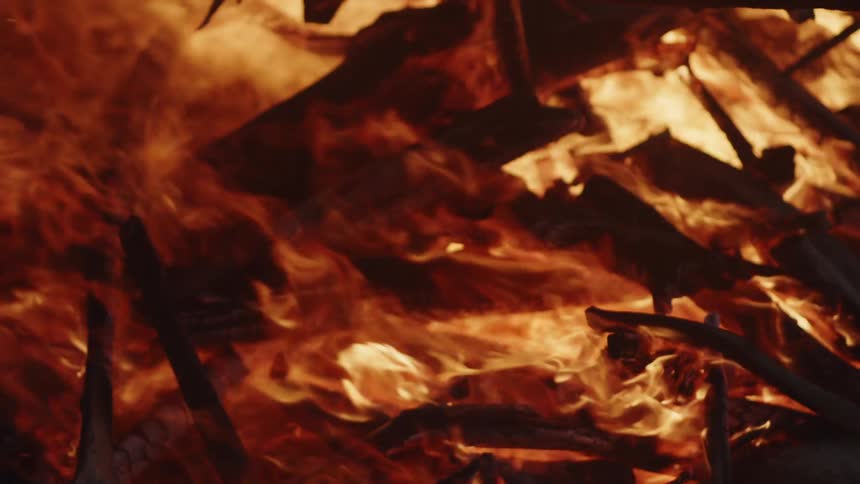 A closeup shot shows intense vibrant flames and burning wood in a bonfire