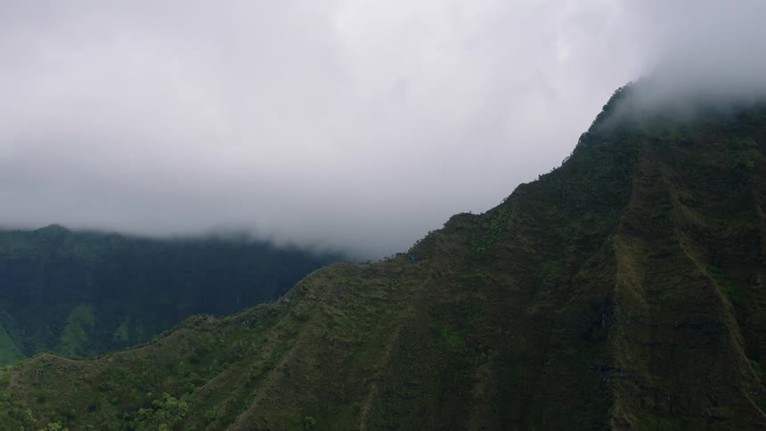 Verdant rugged mountain slopes rise into a misty cloudladen sky partially obscured by the swirling fog