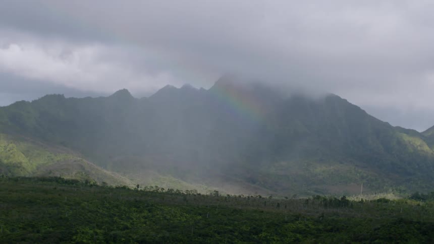 A landscape view shows green mountains under a cloudy sky with peaks partially obscured by mist and low clouds