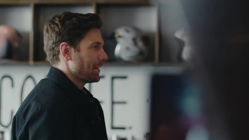 A young handsome man walks into a coffee shop and starts talking to someone