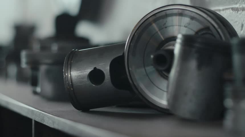 Several engine pistons line a workbench in a dimly lit space with one piston in sharp focus