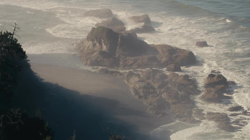 Waves crashing on a rocky coastal shoreline as fog hovers above