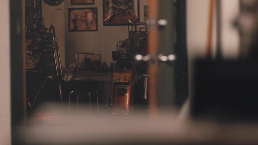 A vintage style garage with a motorcycle featuring a yellow license plate in the center surrounded by framed posters and a warm nostalgic atmosphere