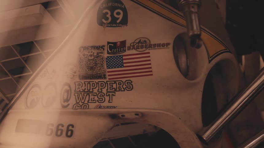 The image shows a closeup of a vintage motorcycle or car body with various stickers hanging from a rack