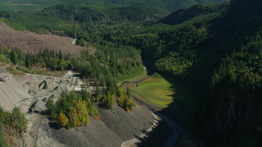 A river valley flanked by forests and a gravel quarry leading to a mountainous landscape crowned by a snow capped peak