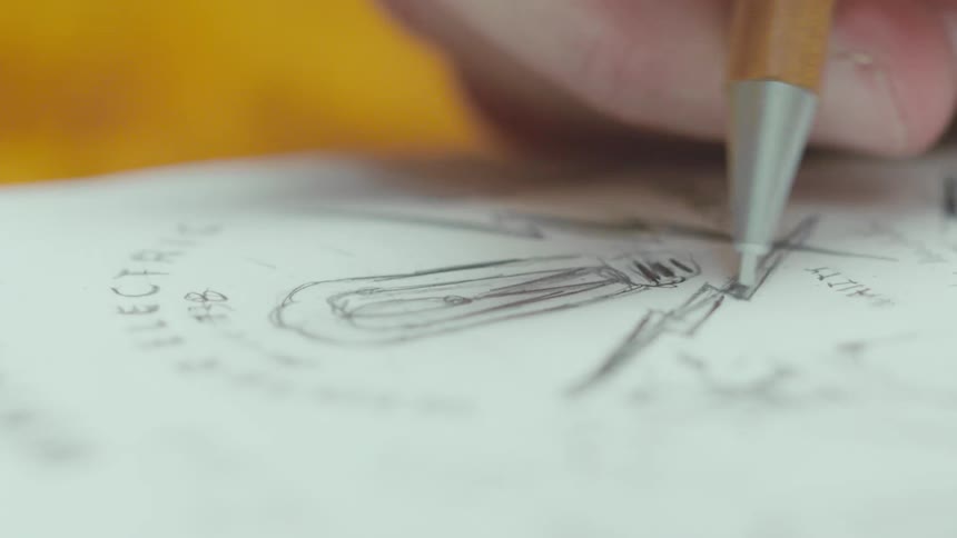 A hand uses a mechanical pencil to sketch an electrical diagram on paper