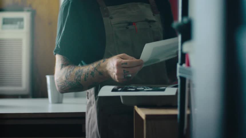 Tattooed hands of a person holding sheets of photographs