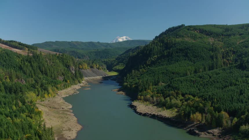 A winding river flows through a deep valley flanked by densely forested slopes with a faint mountain peak visible in the distance
