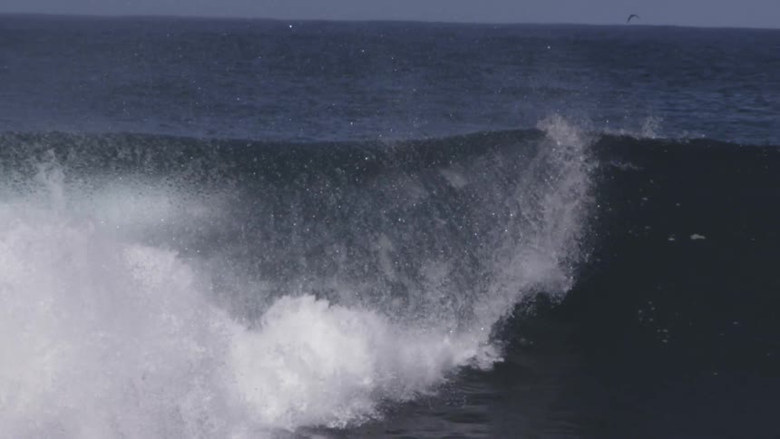 A large wave crashes down on a sunny day