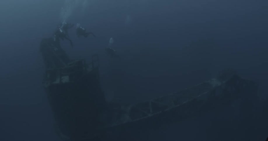 Three divers examine a sunken ship