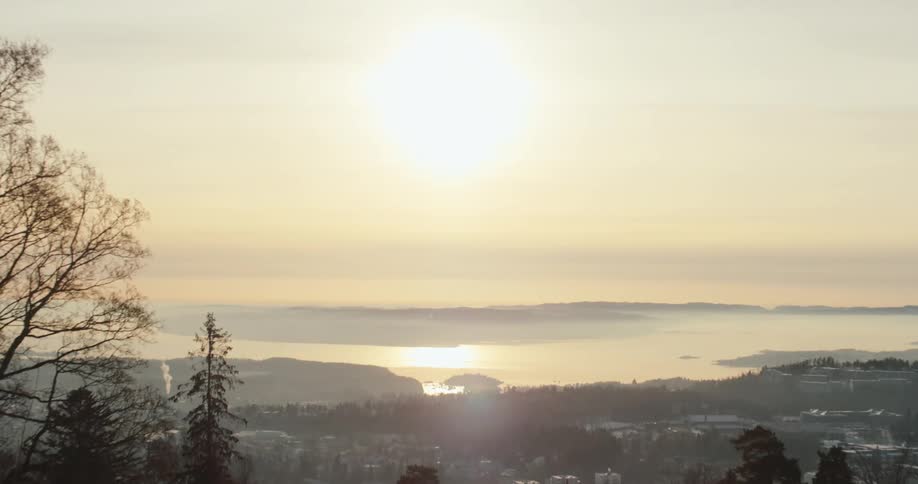A serene sunrise over city nestled between a hilly landscape and a body of water reflecting the sunlight