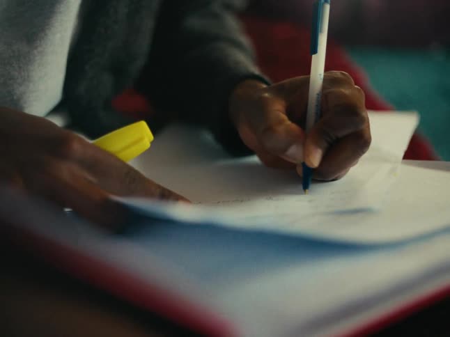 Hands writing on a piece of paper with a blue pen with a yellow highlighter nearby