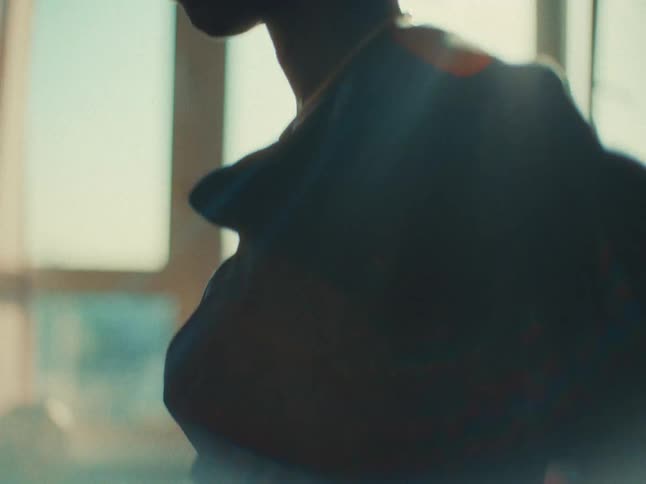 Closeup of a womans torso as she puts on a sweater in a sunlit room with large windows