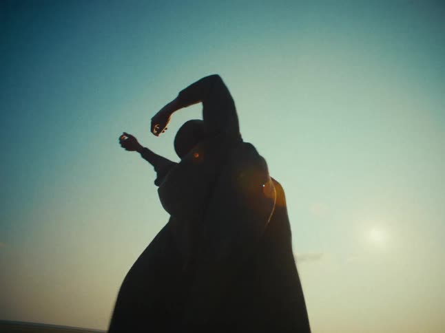 The silhouette of a person with their arms up in the wind