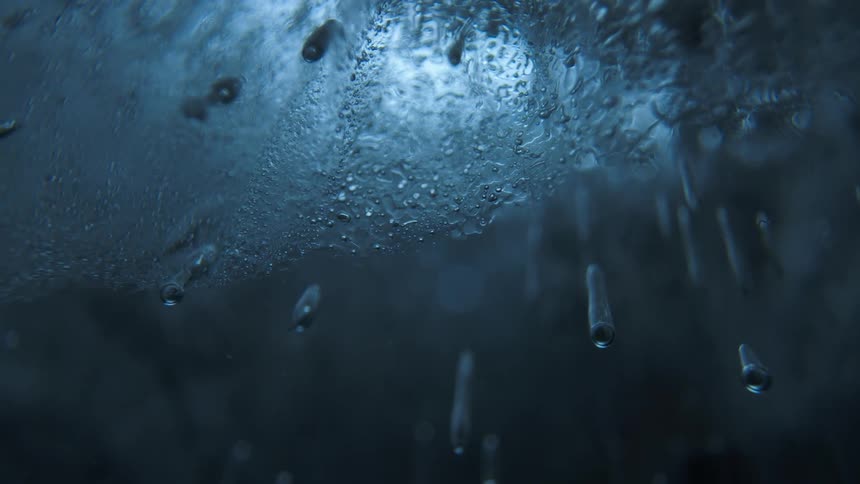 Blue tinted ice displays trapped air bubbles and water droplets creating an abstract textured pattern within the frozen structure