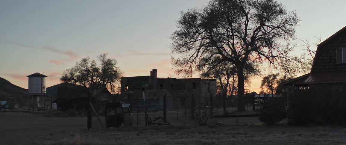 Vehicle scrap sits in the corner of a residential yard in a rural town under a red sky