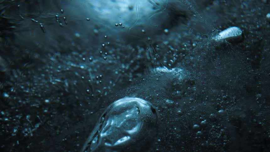 A dark textured surface is covered with small droplets reflecting light and creating a glistening effect