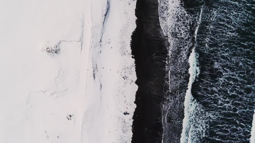 Waves crash onto the beach bordering snow covered terrain