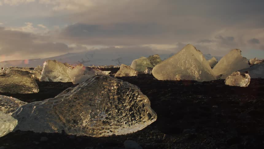 A landscape dotted with jagged chunks of ice under a twilight sky with scattered clouds at sunset