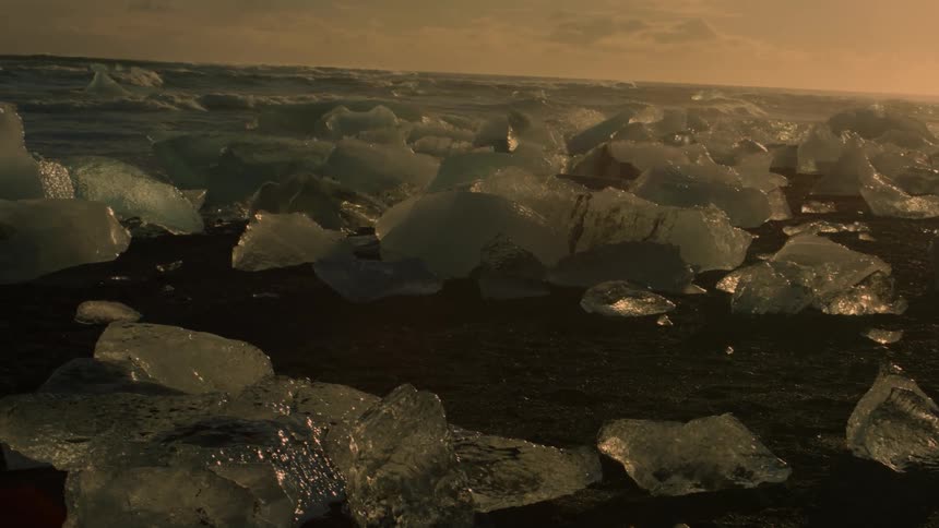 A landscape dotted with jagged chunks of ice under a twilight sky with scattered clouds at sunset