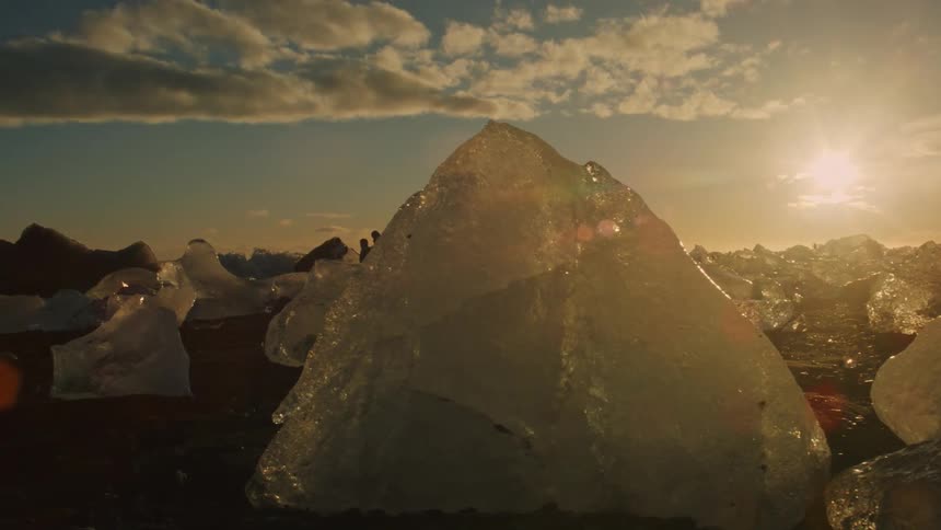 A landscape dotted with jagged chunks of ice under a twilight sky with scattered clouds at sunset