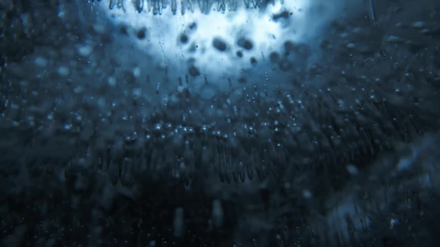 Air bubbles are trapped within a dark blue glass sphere illuminated by soft light from behind
