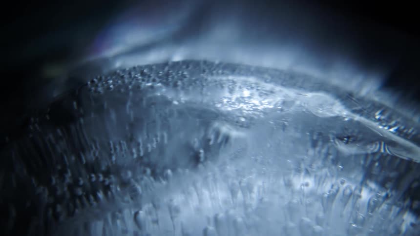 Closeup of a circular glass or ice disk with trapped air bubbles spinning under dim lights