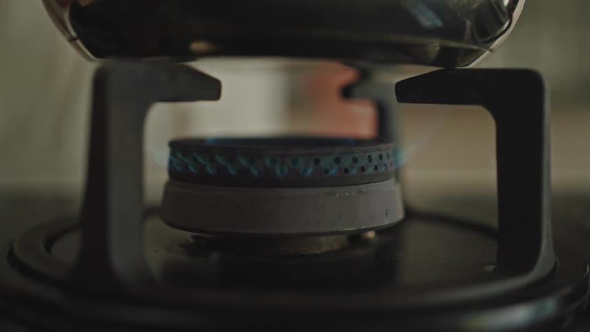 Closeup of a gas stove turning on with a metal pan resting on the blue flame
