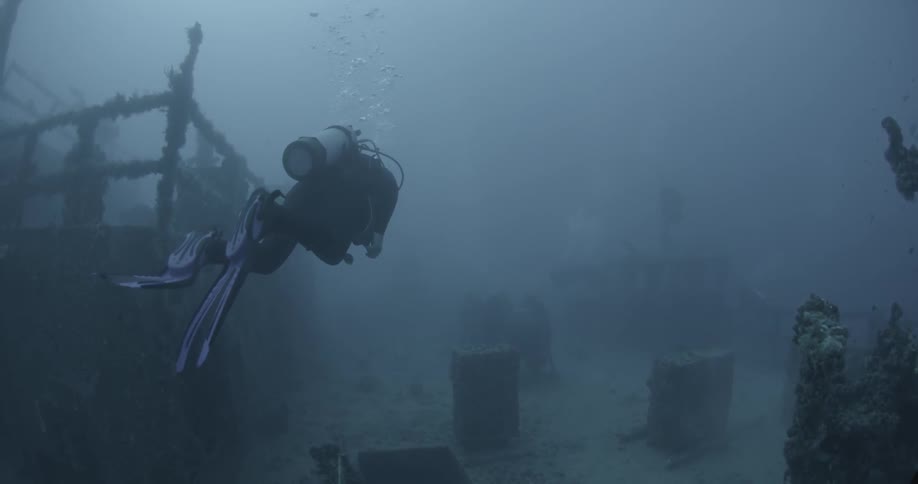 A diver is swimming near an old wreck in the ocean