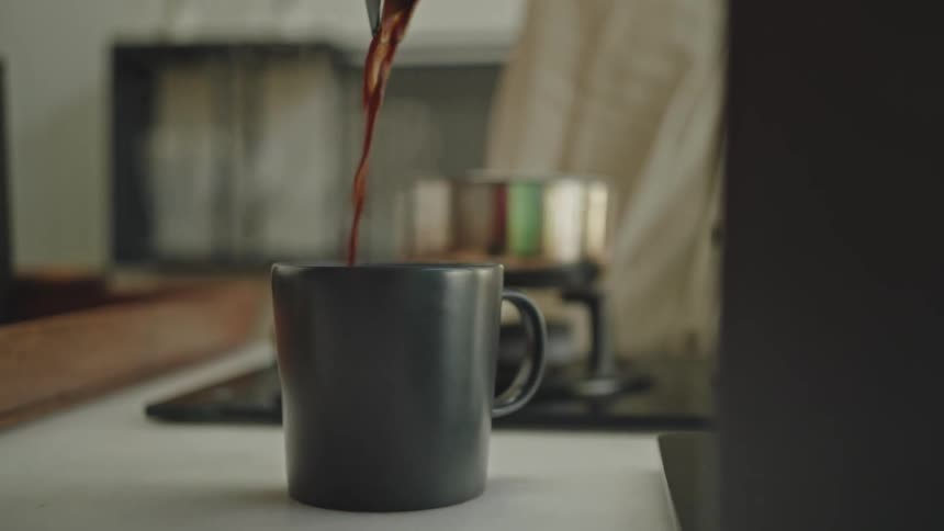 Person pouring coffee from a teapot into a gray mug
