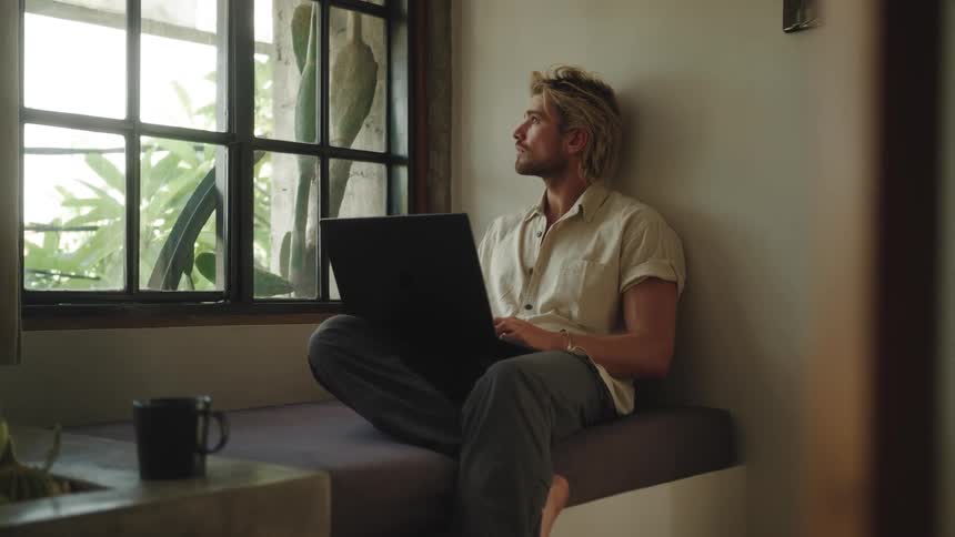 A man is typing on a laptop by the window