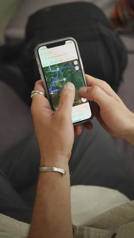 A man is sitting indoors while scrolling through a geographical map on his smartphone
