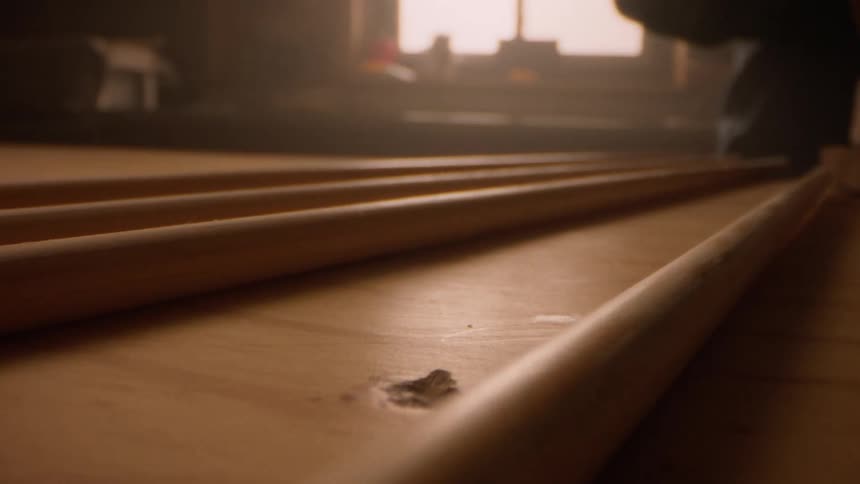 A hand reaches into a dimly lit space selecting a wooden rod from several arranged in a row