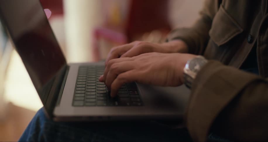 A man sits indoors while talking on his smartphone and typing on his laptop