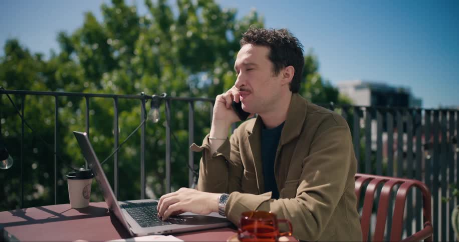 Man talking on cell phone while sitting on a porch in front of his laptop