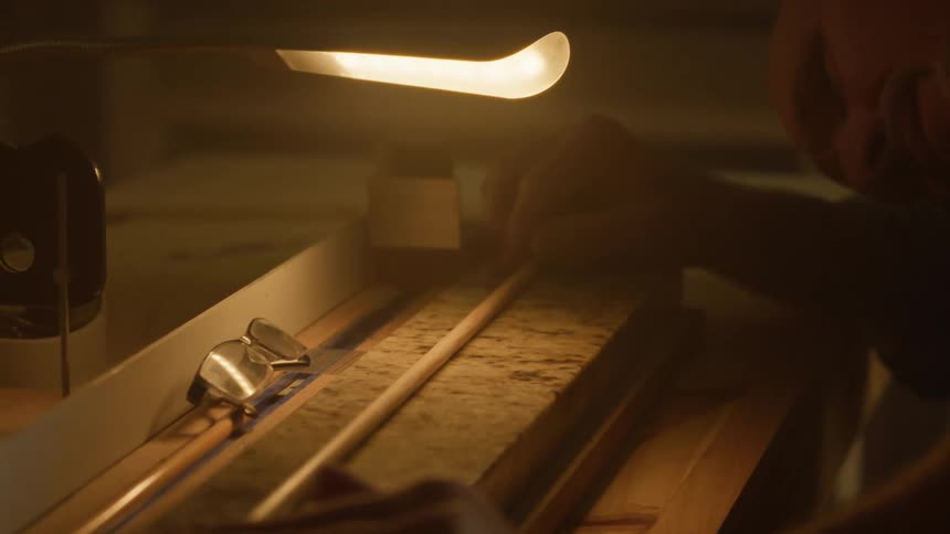 Under a warm light a person works with a long thin object alongside other tools on a textured surface
