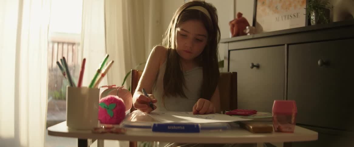 A little girl is sitting and drawing on a piece of paper at a wooden table