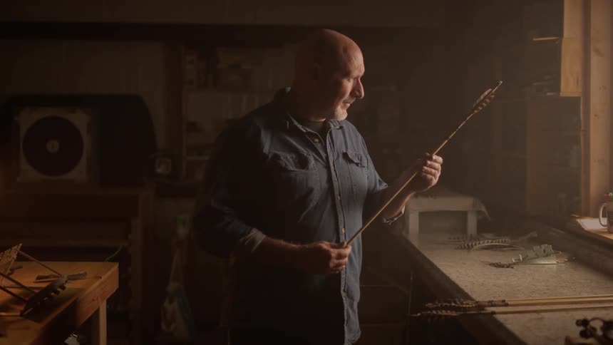 Man standing indoors examining a homemade arrow
