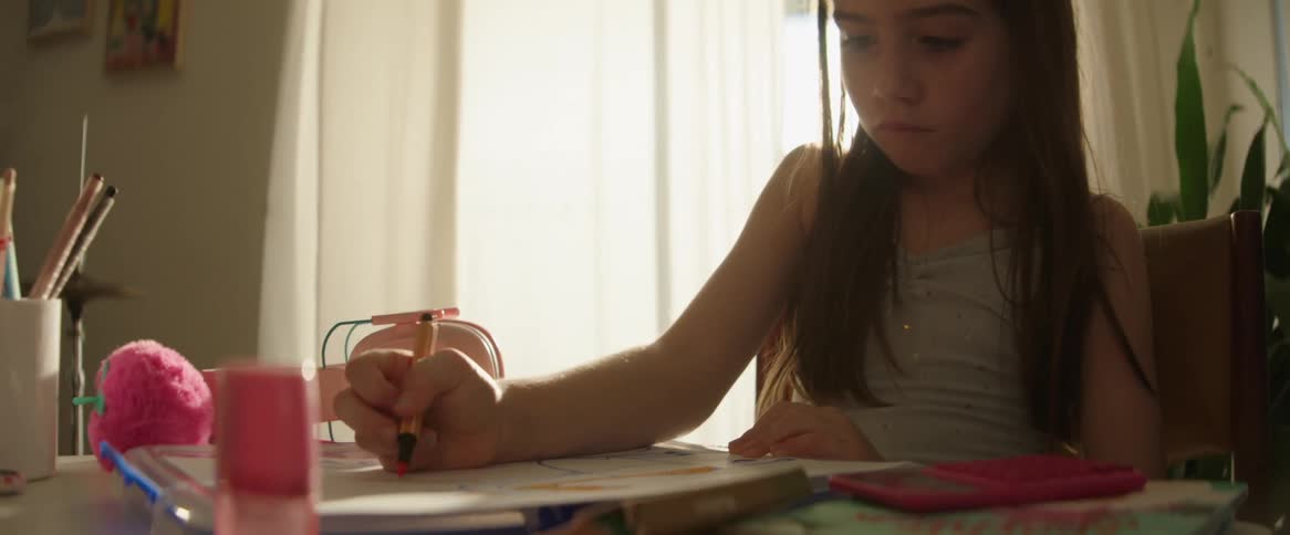 A young girl is sitting indoors while coloring a picture