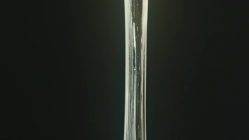 A viscous transparent substance is being stretched vertically against a dark background