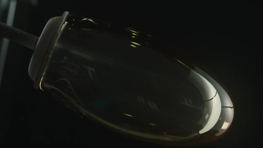 A glass vase is rotated against a dark background capturing the glassblowing process