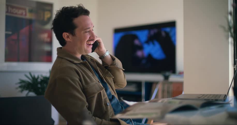 Man smiles while consulting his laptop during a phone call