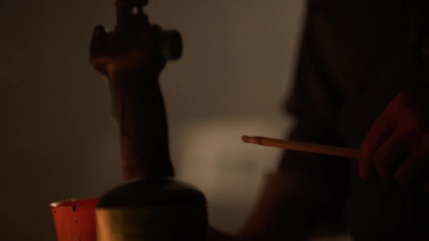A hand is holding small metallic object near the flame of a blowtorch which is emitting a blue flame