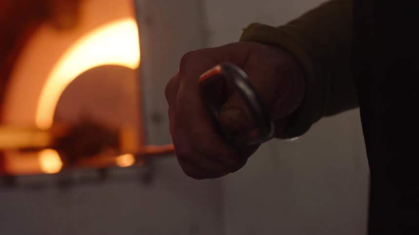 Persons hand holding a metal tool and forging glass onto a sheet metal