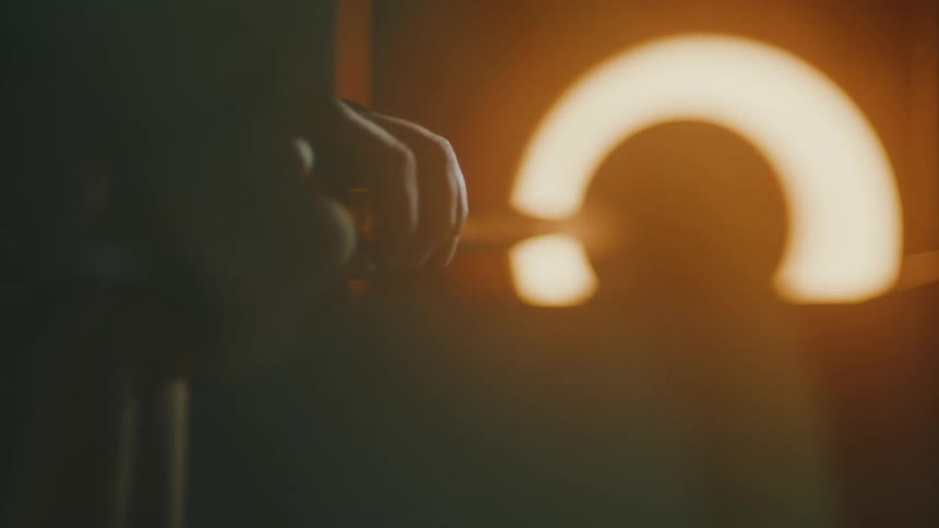 A person using long metal tools to manipulate molten glass inside a glowing hightemperature furnace