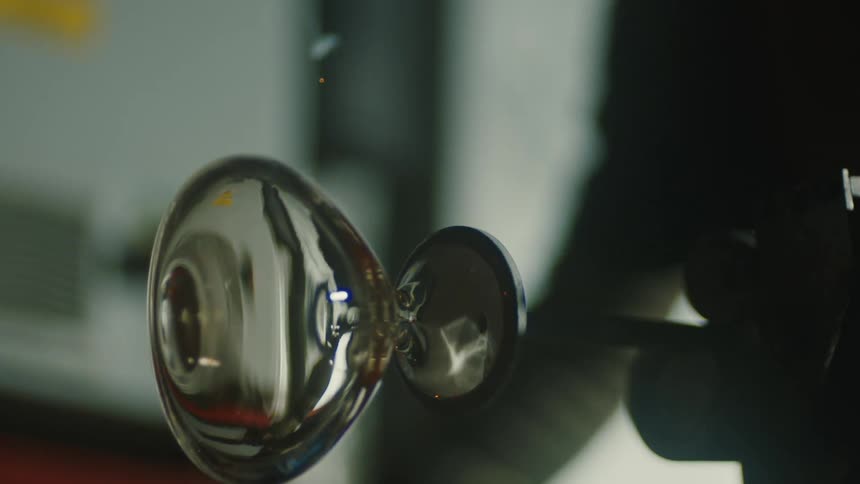 A glass blower shapes molten glass into a vessel creating a smoke effect in a workshop setting