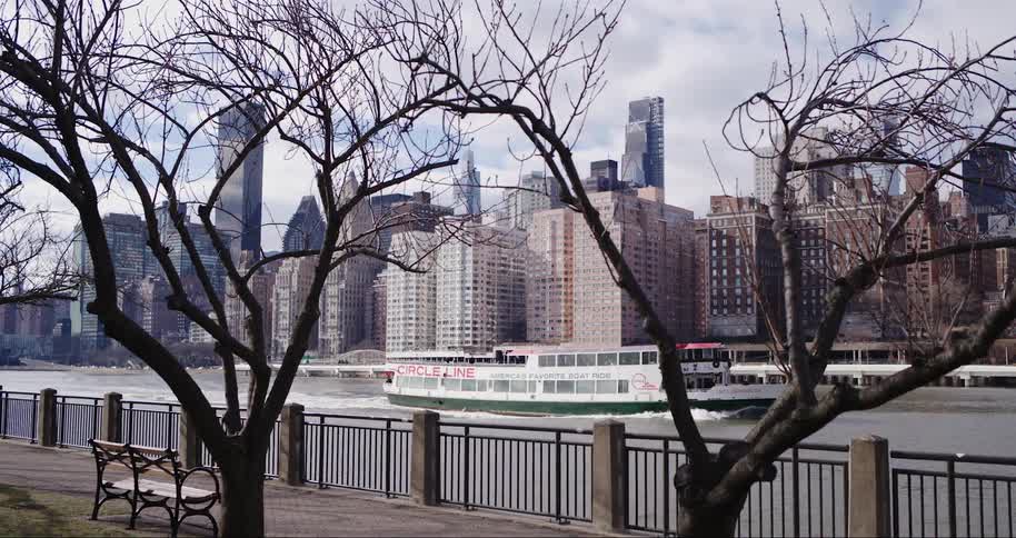 A medium sized boat drives through a lake with a large city in the background