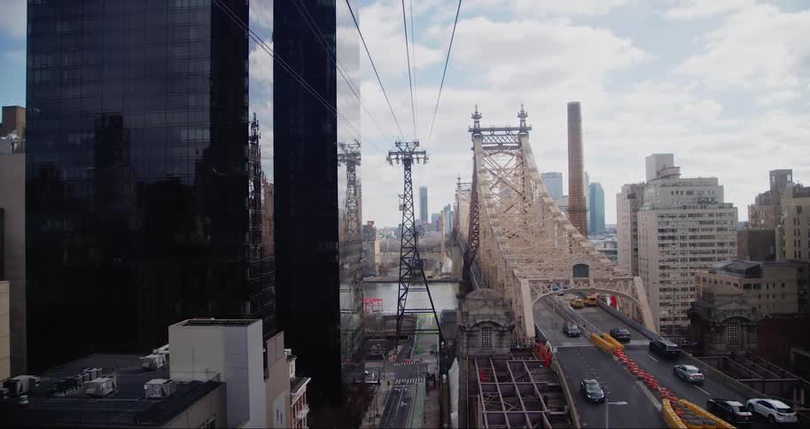 Cityscape of the queensboro bridge in new york city with tall buildings surrounding it and cable car cables crossing the scene